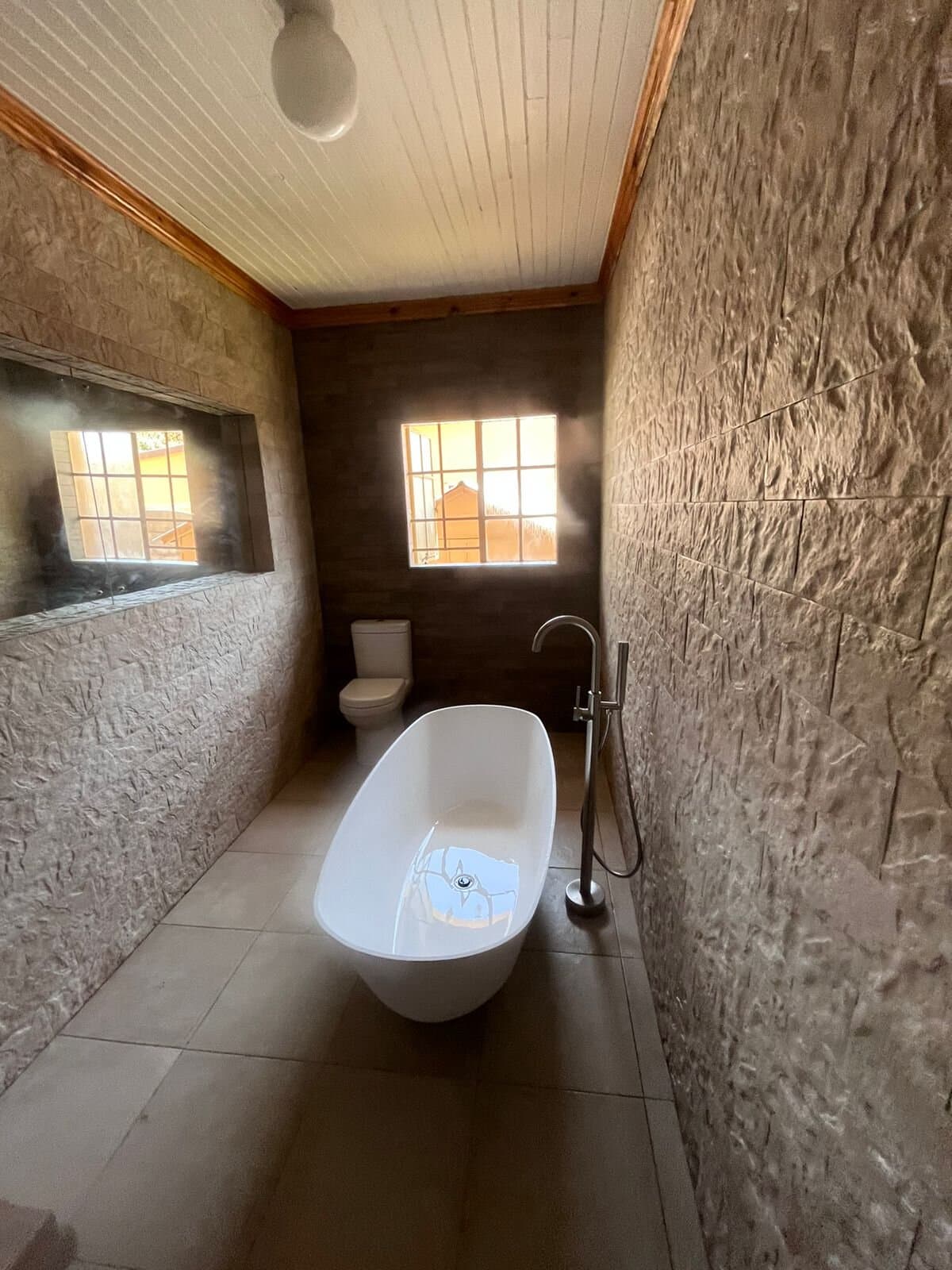 Bathroom renovation with a freestanding bath, textured stone wall and toilet