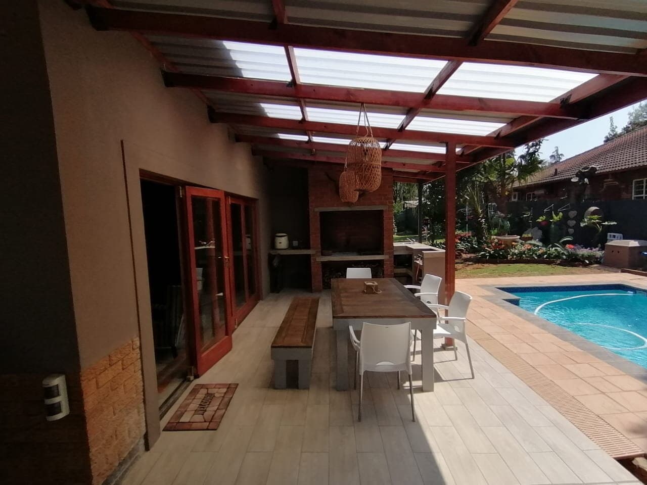 Covered outdoor patio with built-in braai and dining area next to a swimming pool