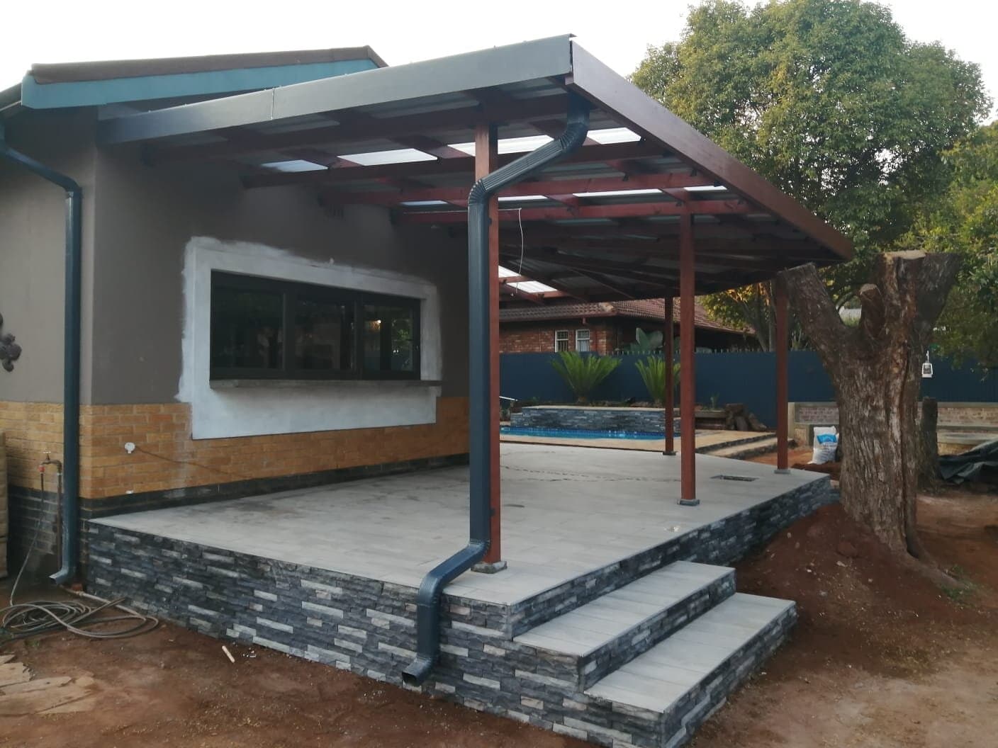 New stone-clad patio deck with a timber pergola roof next to the pool